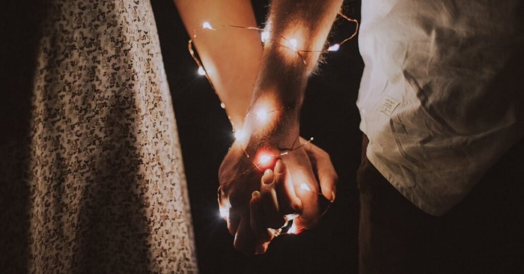 A warm and intimate close-up of a couple holding hands adorned with glowing string lights.